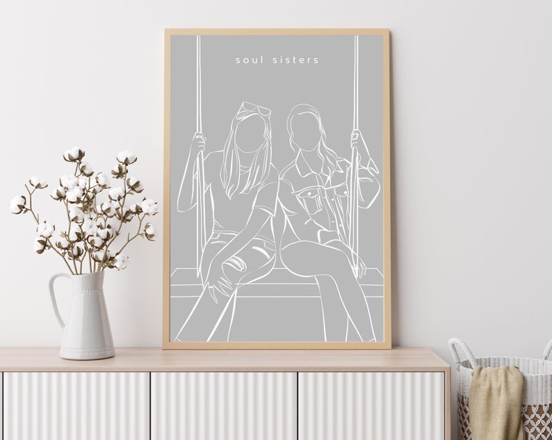 May include: A grey framed print with a white outline drawing of two people sitting on a swing. The text "soul sisters" is at the top of the print.