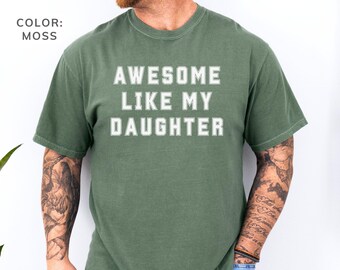 May include: Moss green t-shirt with the text "AWESOME LIKE MY DAUGHTER" in white block letters. The shirt is a solid color and has a crew neck. The color is labeled "MOSS".