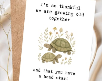 May include: A greeting card with a brown envelope. The white card has the text "I'm so thankful we are growing old together and that you have a head start." Two turtles are illustrated in the center, surrounded by floral elements.