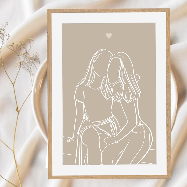 May include: A line art print of two people hugging, with a small heart above them. The print is on a beige background and is framed in a light wood frame.