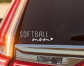 May include: A white vinyl decal with the text "SOFTBALL mom" with a heart symbol after the word "mom" is displayed on the back window of a red car.