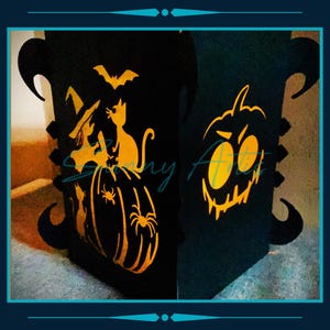 May include: Black Halloween lantern with orange cutouts of a witch, cat, bat, spider, and jack-o'-lantern. The lantern has decorative curved edges and a teal border. The text "Soony Arts" is visible on the lantern.