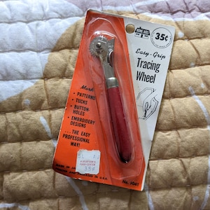 May include: A red and silver tracing wheel with a plastic package that says "Easy-Grip Tracing Wheel" and "35 cents". The package also lists uses for the wheel, such as marking patterns, tucks, button holes, and embroidery designs.