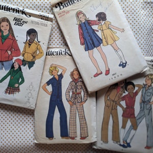 May include: Five vintage sewing patterns for children's clothing. The patterns are from the brand Butterick and feature various styles, including a jacket, a dress, and a jumpsuit. The patterns are printed on white paper with black and red text.