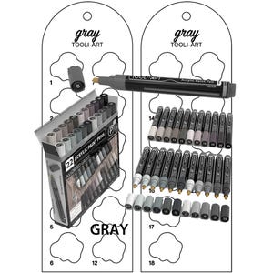 May include: A set of 22 grey acrylic paint pens in a box with the text "22 Acrylic Paint Pens Assorted Greys" on the front. The pens are arranged in a grid pattern and are labelled with numbers 1 through 22. The box is sitting on a white surface with a grey background.