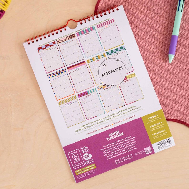 May include: A spiral-bound wall calendar with a white background featuring twelve monthly grid sections in various colorful patterns. The bottom section is purple with white text including the brand name Good Tuesday and recycling icons.