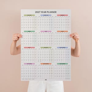 May include: A 2027 year planner wall calendar featuring a grid layout for all twelve months. Each month is labelled with a coloured header bar and contains a standard calendar grid with days of the week listed across the top of each section.