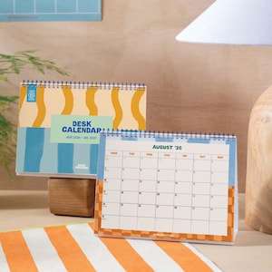 May include: Two desk calendars with blue spiral binding. One calendar displays the text "DESK CALENDAR AUG 2026 - JUL 2027" with a blue and yellow design. The other calendar shows the month of August '26.