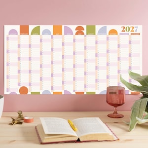 Könnte beinhalten: Ein horizontaler Wandkalender für 2027 mit einem Raster für jeden Monat von Januar bis Dezember. Das Design enthält farbenfrohe geometrische Formen in Orange, Grün, Lila und Hellblau mit übersichtlichen Spalten für die tägliche Planung.