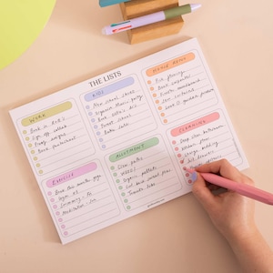 May include: A rectangular paper notepad titled THE LISTS with six color-coded sections labeled WORK, KIDS, HOUSE RENO, EXERCISE, ALLOTMENT, and CLEANING. Each section contains lined rows with circular checkboxes, some filled with handwritten tasks.