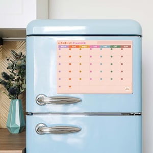 Peut inclure: Un planificateur mensuel magnétique avec un fond pêche et des points colorés pour chaque jour de la semaine. Les jours de la semaine sont étiquetés : Lun, Mar, Mer, Jeu, Ven, Sam, Dim.