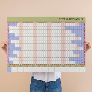 May include: A 2027 year planner wall calendar featuring a grid layout with months listed horizontally and days vertically. The design includes alternating light pink and white columns for dates, with light blue blocks indicating weekends.