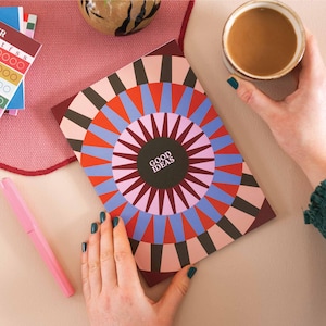Peut inclure: Un carnet rouge, rose, bleu et marron avec un motif géométrique et le texte "GOOD IDEAS" dans un cercle noir au centre.