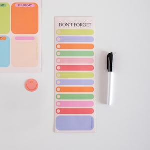 Può includere: Un blocco note bianco con le parole "DON'T FORGET" e linee orizzontali colorate. Un pennarello nero e un adesivo con la faccina sorridente sono anche nell'immagine. Il blocco note è per promemoria e appunti.
