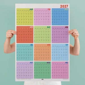 May include: A 2027 wall calendar featuring a grid layout with twelve distinct color-coded monthly sections. Each month is displayed in a square block with a grid for dates, labeled with the month name in bold text at the top right of each section.