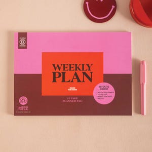 Può includere: Un blocco per la pianificazione settimanale rosa e marrone con le parole "WEEKLY PLAN" in grandi lettere arancioni. L'agenda include un pianificatore settimanale, una lista di cose da fare, un tracker delle abitudini e note. Una penna rosa è accanto all'agenda.