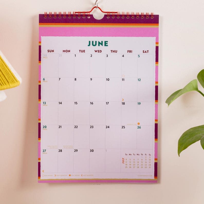 May include: A wall calendar for the month of June featuring a white grid with dark red text for days of the week and dates. The border has horizontal stripes in pink, yellow, and purple. It is held together by a red spiral wire at the top.