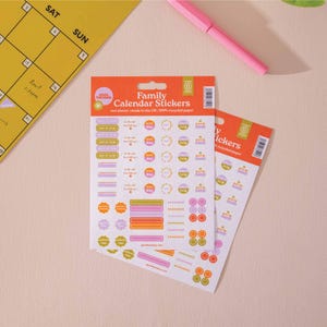Könnte beinhalten: Zwei Blätter mit bunten Familienkalender-Aufklebern mit verschiedenen Designs, darunter "Schuljahresende", "Geburtstag", "Ferien", "Reise" und "Party". Die Aufkleber sind auf weißem Hintergrund mit einem rosa-gelben Farbschema.