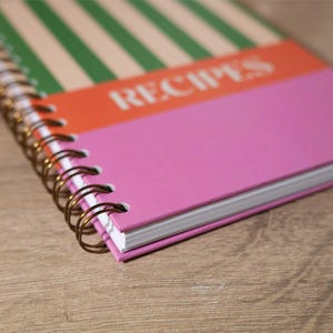 May include: A pink, orange, and green striped spiral bound notebook with the word "RECIPES" printed on the cover.