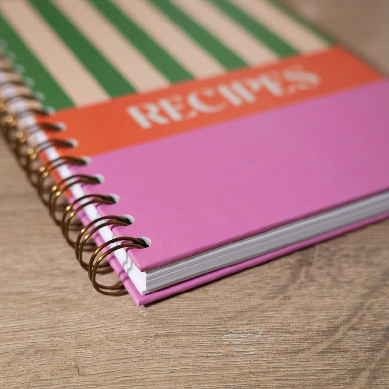 May include: A pink, orange, and green striped spiral bound notebook with the word "RECIPES" printed on the cover.