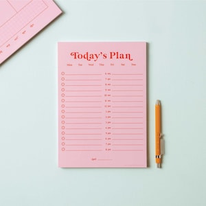 May include: A pink notepad with the words "Today's Plan" in red script. The notepad has a daily schedule layout with time slots and star-shaped icons. An orange pen rests on the right side of the notepad.