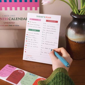 Peut inclure: Un agenda quotidien avec un schéma de couleurs vert et rose. L'agenda comporte une section pour les tâches prioritaires et un horaire pour la journée. L'agenda est ouvert à la page du plan du jour et comporte une section pour les tâches de demain.