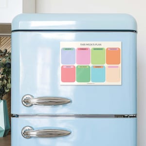 May include: A weekly planner magnet with pastel-colored boxes for each day of the week, labeled Monday through Sunday. The text "THIS WEEK'S PLAN" is at the top. The magnet is attached to a light blue refrigerator.