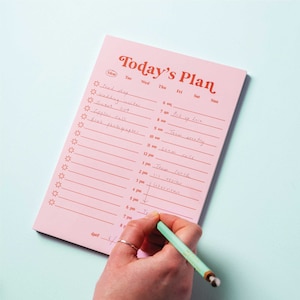 May include: A pink notepad with a red title "Today's Plan" and a daily planner layout. The notepad has a list of tasks written in black ink, including "wedding invites", "pick up Liam", and "team meeting".