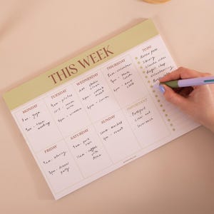 May include: A weekly planner notepad with a pale green header labeled THIS WEEK in brown text. The grid features columns for each day of the week and a TO DO list section with bullet points. Handwritten notes fill the daily slots and the list.
