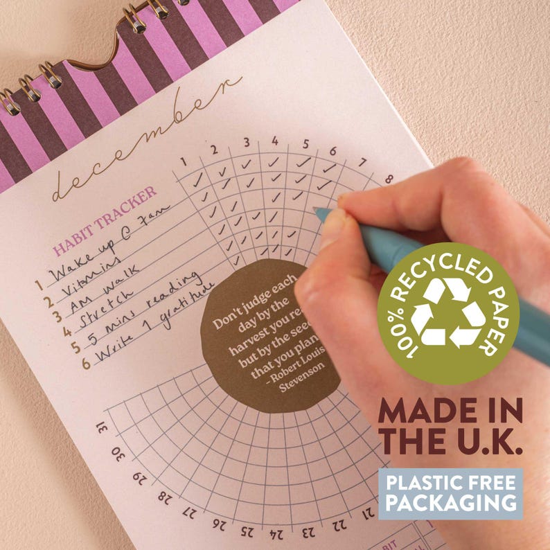 May include: A habit tracker notebook open to December, with a hand using a blue pen to mark a check. The notebook has a spiral binding and a brown and pink striped design. The text "100% Recycled Paper" and "Made in the U.K." are visible.
