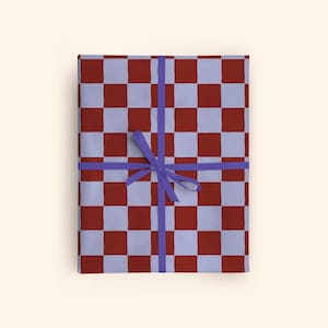 May include: A present wrapped in red and light blue chequered paper, tied with a purple ribbon. The gift is rectangular and rests on a cream-coloured background. The wrapping paper has a grid pattern.