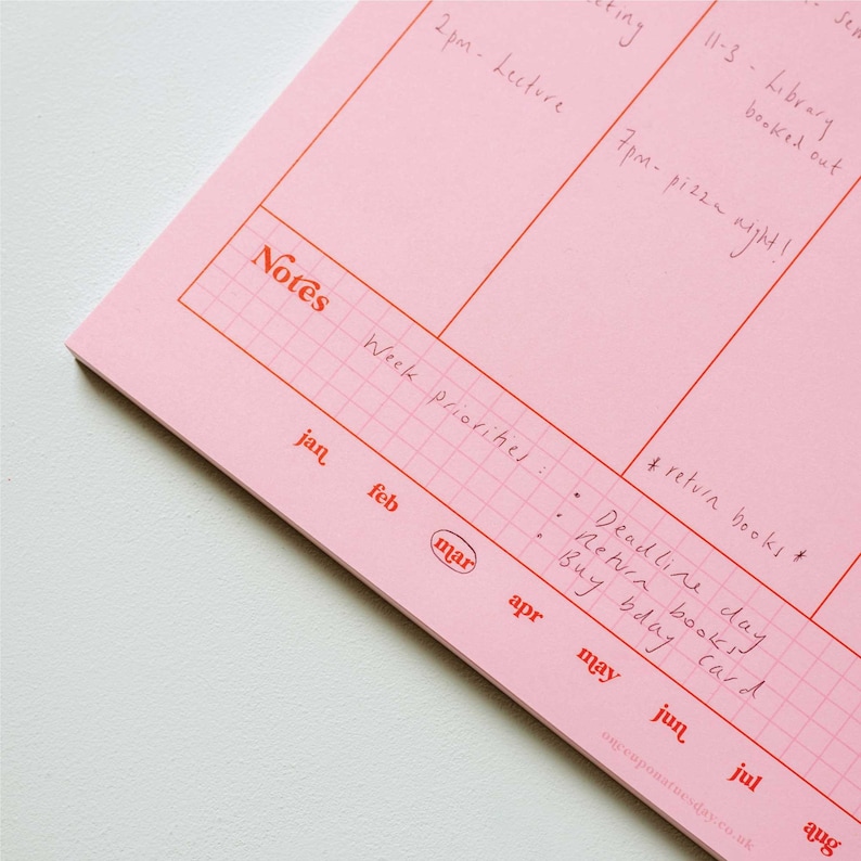 May include: A pink weekly planner with a grid pattern and red lines. The planner has a section for notes and a section for weekly priorities. The months of January through August are listed at the bottom of the planner. The text "Notes" is written in red at the top of the planner. The text "Week priorities" is written in black at the top of the planner. The text "# return books" is written in black at the bottom of the planner. The text "Deadline day" is written in black at the bottom of the planner. The text "Return books" is written in black at the bottom of the planner. The text "Buy bday card" is written in black at the bottom of the planner.