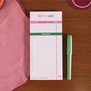 Könnte beinhalten: Ein weißer To-Do-Liste-Notizblock mit rosa, grünen und roten Akzenten. Der Notizblock hat einen Abschnitt für "Must Do Today" und "The Rest". Der Notizblock hat auch den Text "Work Hard, Play Nice" unten.