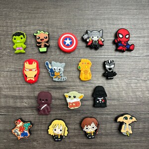 May include: A collection of 15 colorful cartoon character shoe charms featuring characters from popular movies and TV shows, including Marvel, Star Wars, and Harry Potter. The charms are made of rubber and have a variety of colors and designs.