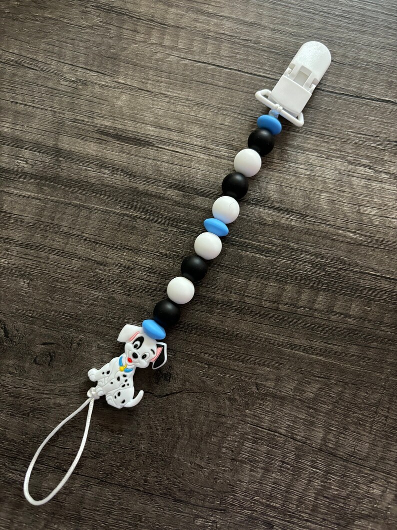 Peut inclure: Un attache-sucette en silicone blanc avec des perles noires et bleues et un charme de chien dalmatien.