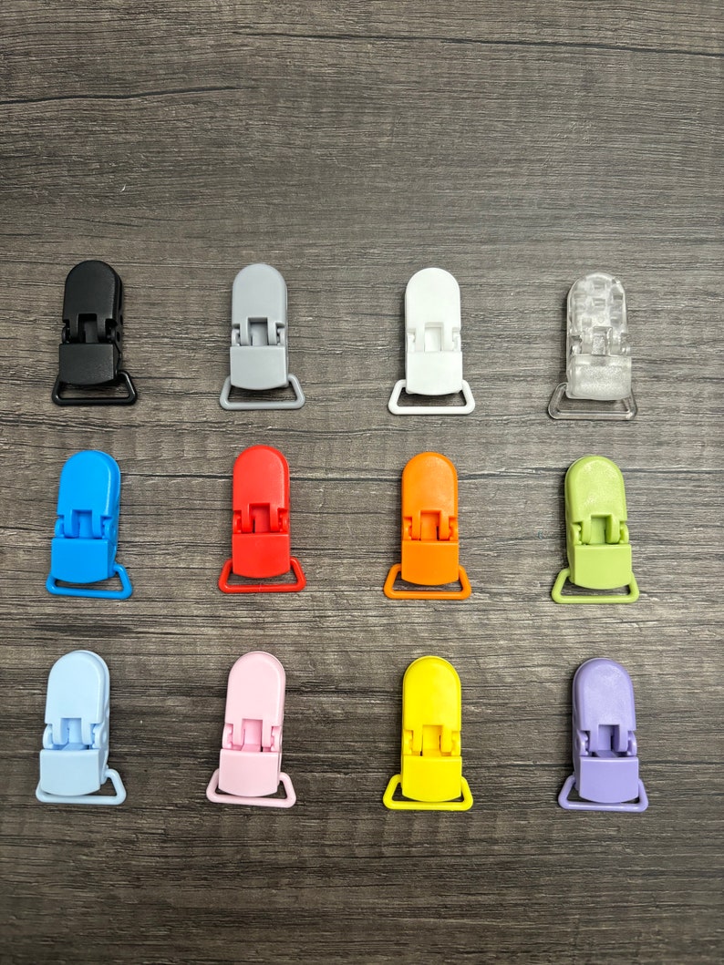 May include: Assortment of 12 plastic baby pacifier clips in various colors, including black, gray, white, blue, red, orange, green, light blue, pink, yellow, purple, and clear.