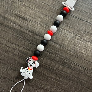 Peut inclure: Un hochet pour b&eacute;b&eacute; en silicone noir, blanc et rouge avec un charme de chien dalmatien. Le hochet a un clip pour l'attacher aux v&ecirc;tements.