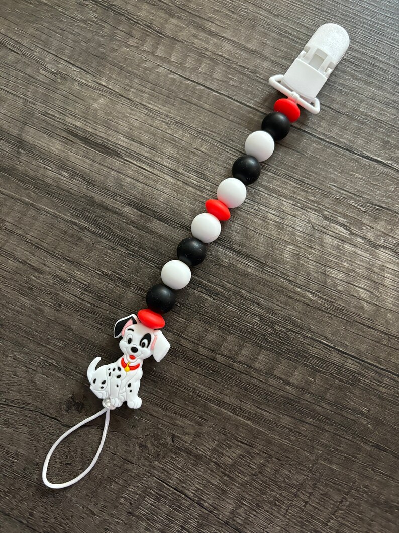 Peut inclure: Un hochet pour b&eacute;b&eacute; en silicone noir, blanc et rouge avec un charme de chien dalmatien. Le hochet a un clip pour l'attacher aux v&ecirc;tements.