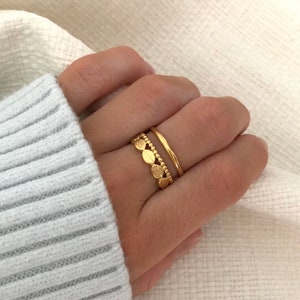 Puede incluir: Dos anillos de oro en un dedo. Un anillo es una banda simple, el otro es una banda con una fila de pequeños discos redondos texturizados.