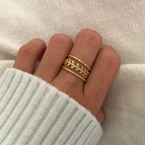Peut inclure: Bague en or avec un délicat motif de feuilles. La bague est composée de trois bandes, chacune avec un motif différent.