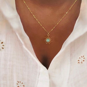 Op de afbeelding: Een gouden ketting met een delicate zon hanger met een lichtblauwe edelsteen.