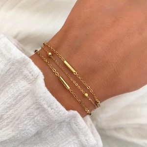 Könnte beinhalten: Ein Set aus drei goldenen Kettenarmbändern mit kleinen runden Perlen und dünnen Balkenakzenten.