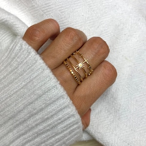 Peut inclure: Un ensemble de quatre bagues en or avec un motif en forme d'étoile. Les bagues sont empilées sur un doigt.