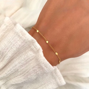 Peut inclure: Un bracelet délicat en chaîne dorée avec de petits accents ronds.