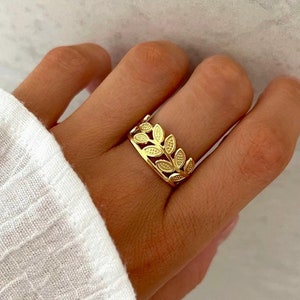 Peut inclure: Une bague en or avec un motif de feuilles. La bague est portée au doigt.