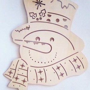 May include: A wooden snowman ornament with a top hat and scarf. The snowman's face has a carved-out smile and button eyes. The scarf and hat are decorated with carved-out snowflakes and other festive designs. A string is attached for hanging.