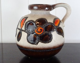 May include: A white ceramic vase with a brown and orange floral design. The vase has a round body and a handle.