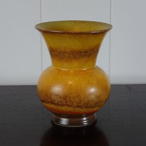 以下が含まれることがあります： 黄色と茶色のセラミック製の壺で、上部は広がり、胴体は丸みを帯びています。壺は、黄色、オレンジ、茶色のグラデーションがかった釉薬で覆われています。