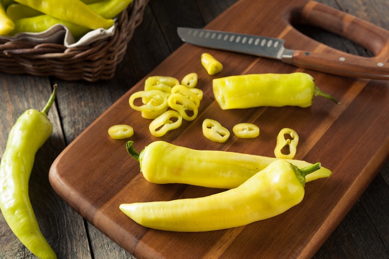 May include: A wooden cutting board with a yellow pepper, a knife, and sliced yellow peppers. The peppers are arranged in a row on the board.