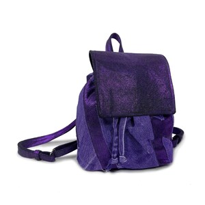Puede incluir: Una pequeña mochila morada de tejido vaquero y tejido brillante. La mochila tiene un cierre de cordón y una solapa con hebilla.